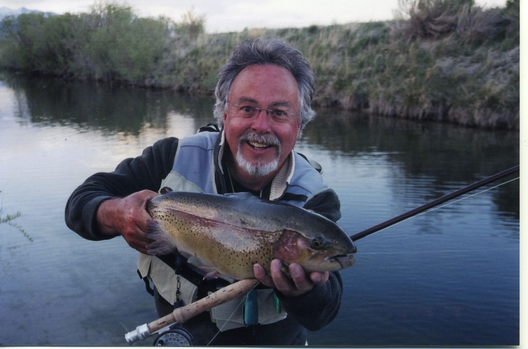 Man holding freshly caught trout in a river with evergreen forest background