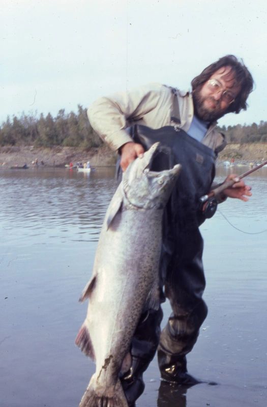 Vintage photo of a man holding a large salmon while standing in shallow water